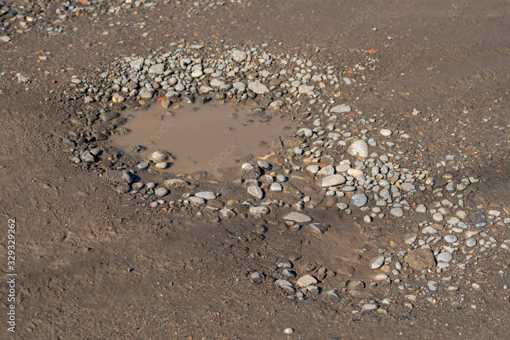 A bumpy wet gravel road after the rain, gravel road is full of potholes A bumpy wet gravel road after the rain, gravel road is full of potholes