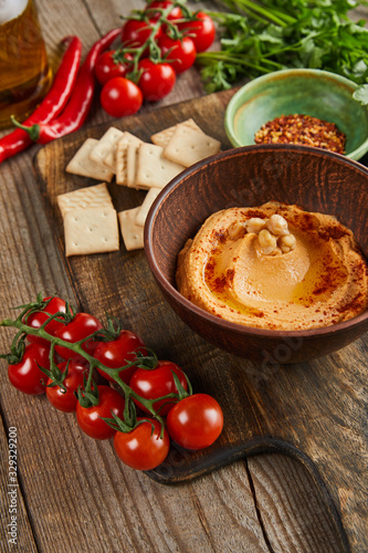 Selective focus of bowls with hummus and spices, ripe vegetables and crackers on wooden background