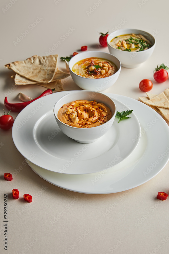 Selective focus of plates and bowls with hummus, fresh vegetables and pita bread on grey