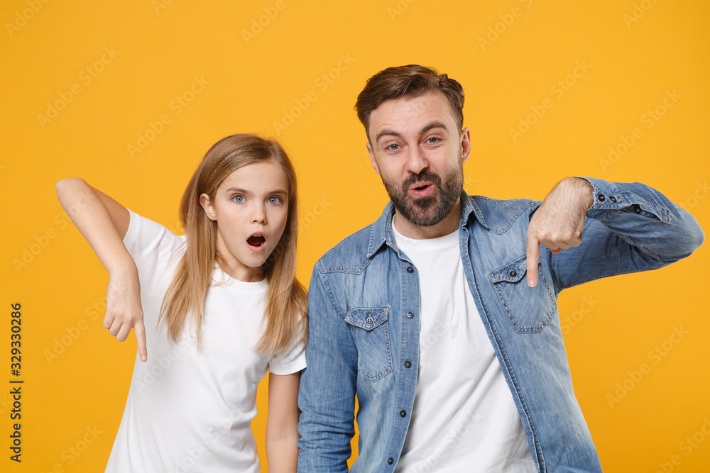 Fototapeta premium Shocked bearded man in casual clothes have fun with child baby girl. Father little kid daughter isolated on yellow background. Love family day parenthood childhood concept. Point index fingers down.