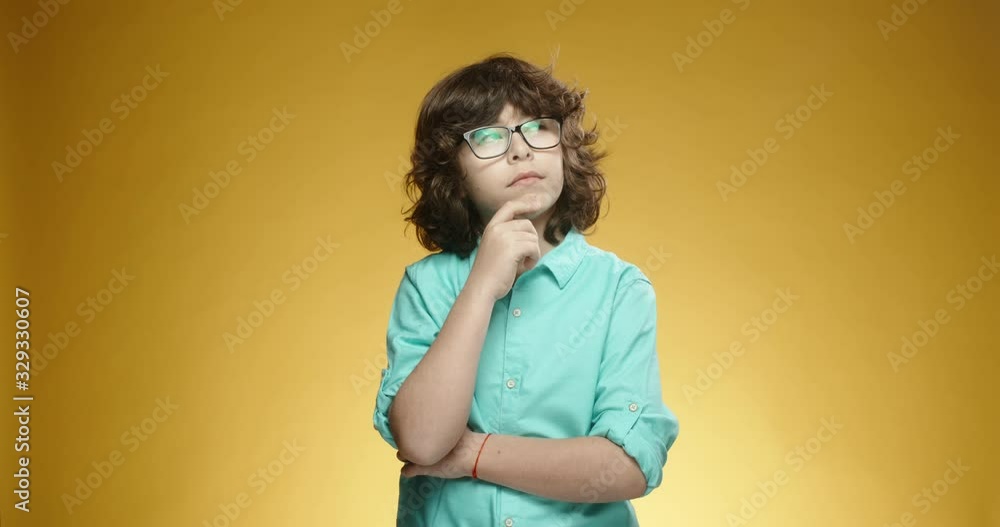 Cute caucasian boy looking at camera and thinking about something, isolated on yellow background - emotions concept close up 4k slow motion Cute caucasian boy looking at camera and thinking about something, isolated on yellow background - emotions concept close up 4k slow motion
