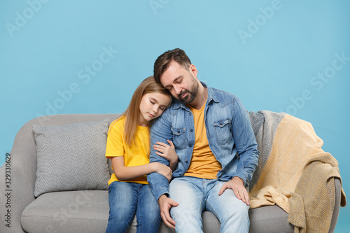 Relaxed bearded man in casual clothes with child baby girl. Father little kid daughter isolated on pastel blue wall background. Love family parenthood childhood concept. Sit on couch hugging sleeping.