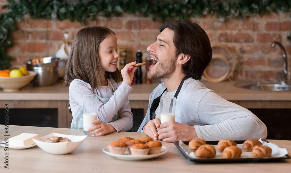 Caring little girl feeding her father with cookies in kitchen Caring little girl feeding her father with cookies in kitchen