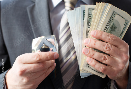 Businessman in suit, tie holds in hands drop of black oil of Brent brand in crystal cube.Pack of hundred dollars bills.Crisis in financial market,falling,rising prices,quotes,changes in exchange rate