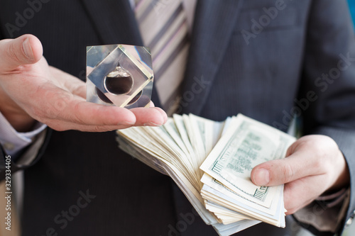 Businessman in suit, tie holds in hands drop of black oil of Brent brand in crystal cube.Pack of hundred dollars bills.Crisis in financial market,falling,rising prices,quotes,changes in exchange rate