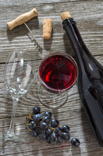 Wine bottle, glass of wine, bunch of blue grapesand and corkscrew photo