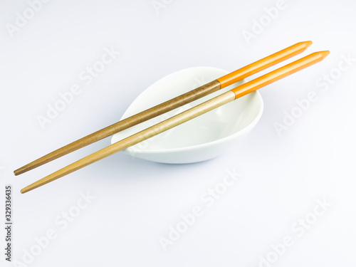 Light brown bamboo chopsticks the base of the handle is orange. Put on a white ceramic cup. And placed on a white ground is a form of eating food for Asians, Chinese, Japanese, Korean, Hong Kong