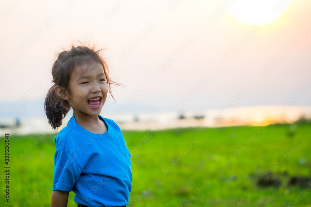 Asian girl kindergarten children wear blue shirts, standing, playing at the water's edge when the sun is about to set. Asian girl kindergarten children wear blue shirts, standing, playing at the water's edge when the sun is about to set.