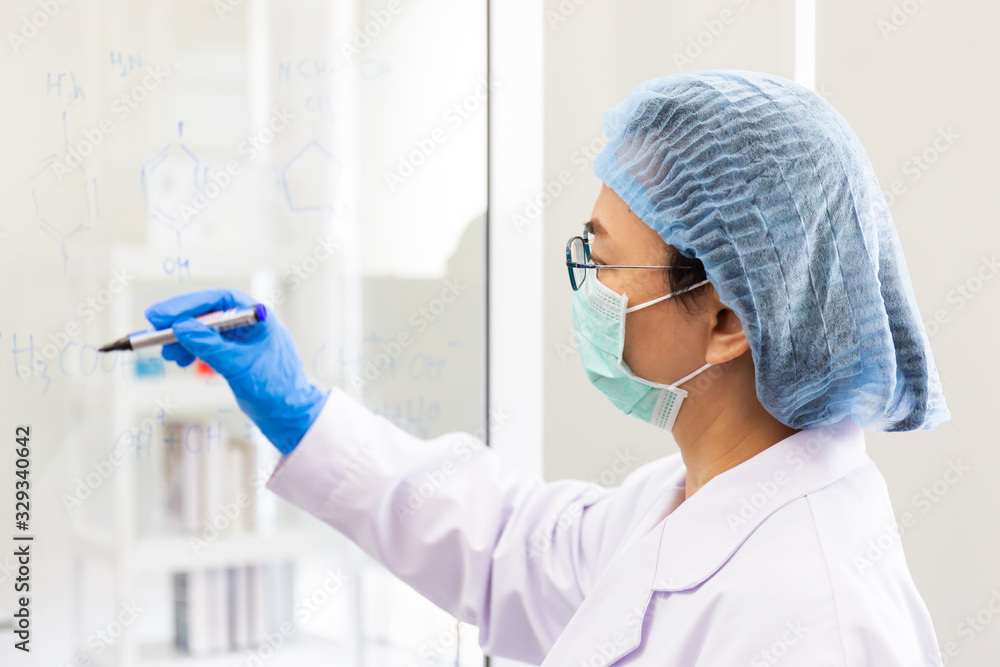 Naklejka premium An Asian female scientist is writing down the formula for calculating chemistry on clear glass in a lab.