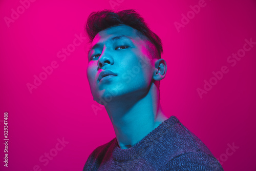 Portrait of a guy with colorful neon light on pink studio background. Male model with calm and serious mood. Facial expression, cyberpunk, millenials lifestyle and look like. Future, technologies.