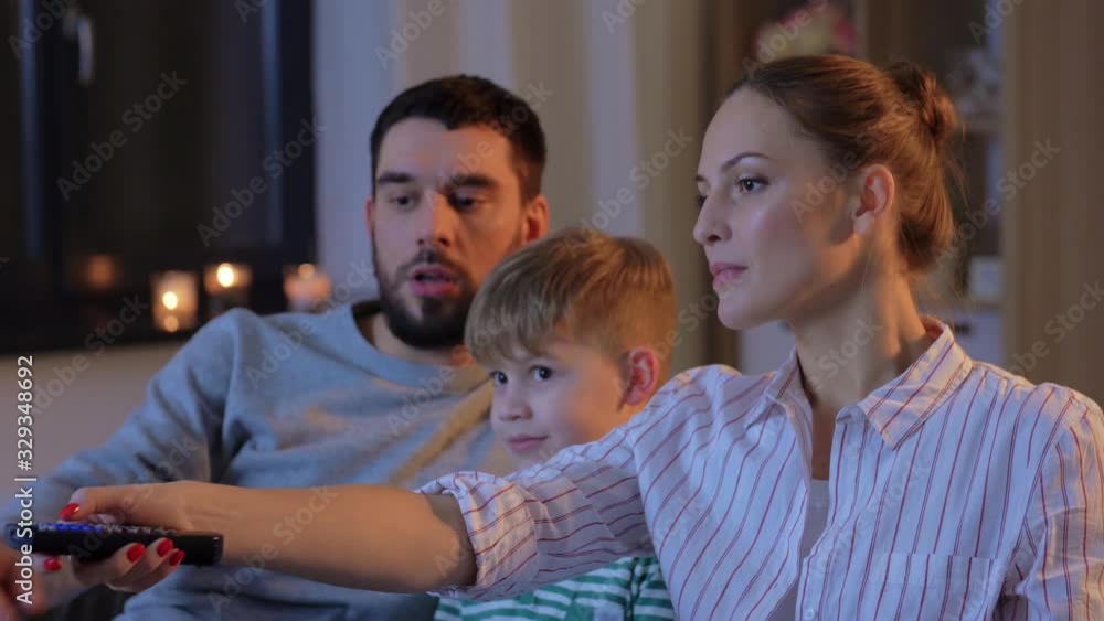 family, leisure and people concept - father, mother and little son with remote control watching tv at home at night family, leisure and people concept - father, mother and little son with remote control watching tv at home at night