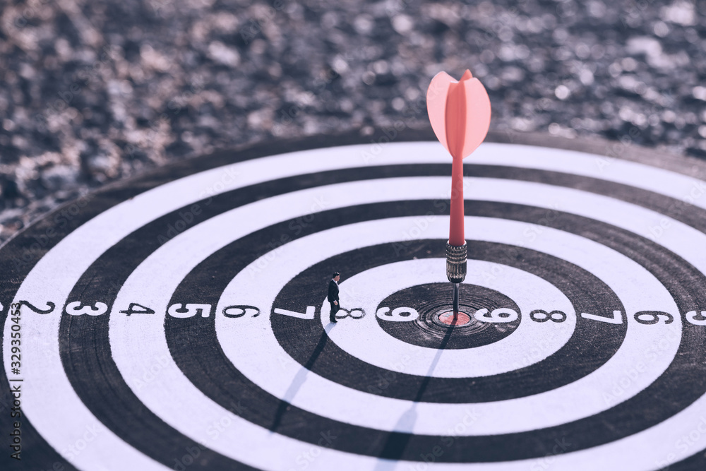 Businessman standing lookup red dart arrow hitting target centre dartboard on sunset background. Business targeting and focus. Businessman standing lookup red dart arrow hitting target centre dartboard on sunset background. Business targeting and focus.