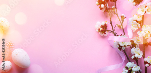 Art Easter banner with painted eggs and spring flowers on light pink background. Top view  flat lay with copy space.