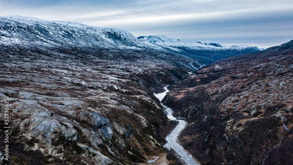 Aura river catting its' way through the deep canyon cut over centuries. Stark, barren tundra landscape stretches up to the horizon. Hills covered with fresh snow. Snowy dark clouds hand above. Aura river catting its' way through the deep canyon cut over centuries. Stark, barren tundra landscape stretches up to the horizon. Hills covered with fresh snow. Snowy dark clouds hand above.