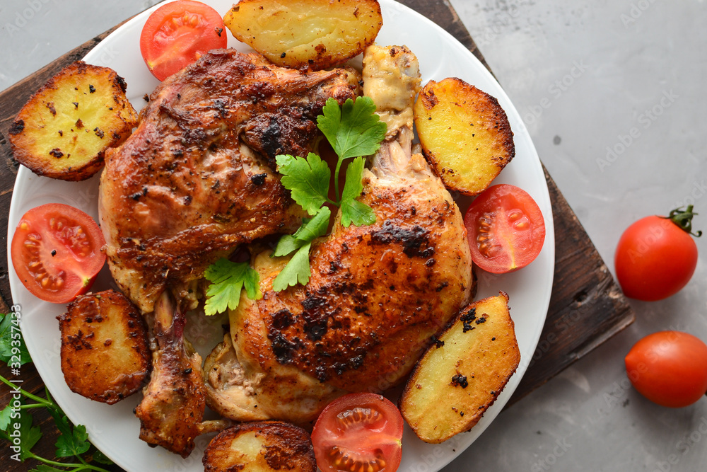 Fried chicken thigh, baked chicken leg. Top view. Dark background. Plate on a wooden board. Baked potatoes, tomatoes and chicken, a delicious lunch. Fried chicken thigh, baked chicken leg. Top view. Dark background. Plate on a wooden board. Baked potatoes, tomatoes and chicken, a delicious lunch.