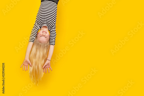 Fotografía Excited crazy little blonde girl hanging happy upside down hands up over isolated yellow studio background