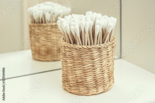 eco-friendly cotton buds made of plant materials are in a wicker basket on a shelf in the bathroom. reed and cotton.