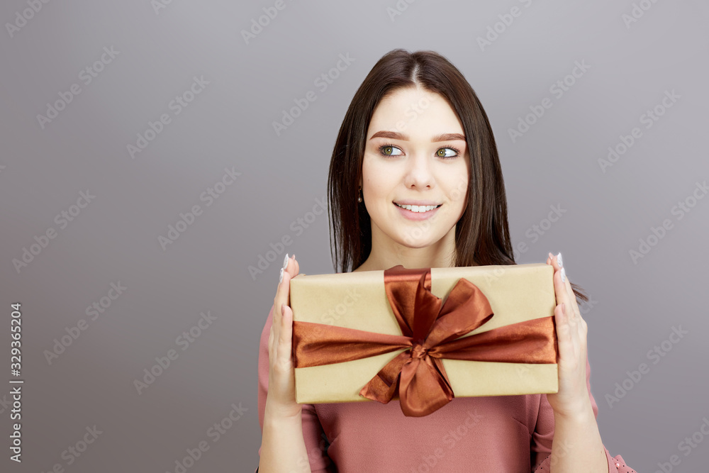 Brunette girl with a New Year's gift in her hands. A young brunette girl with a beautiful wide smile holds a surprise gift for holiday in her hands. Brunette girl with a New Year's gift in her hands. A young brunette girl with a beautiful wide smile holds a surprise gift for holiday in her hands.