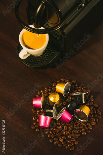 Cup of coffee amd coffee machine in woodden background with coffee capusles ands coffee beans