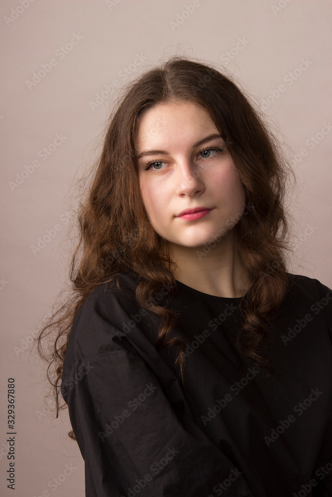 Beautiful elegant young girl with curly wavy long hair brunette in black clothes sweater jacket sitting on a chair in the studio Beautiful elegant young girl with curly wavy long hair brunette in black clothes sweater jacket sitting on a chair in the studio