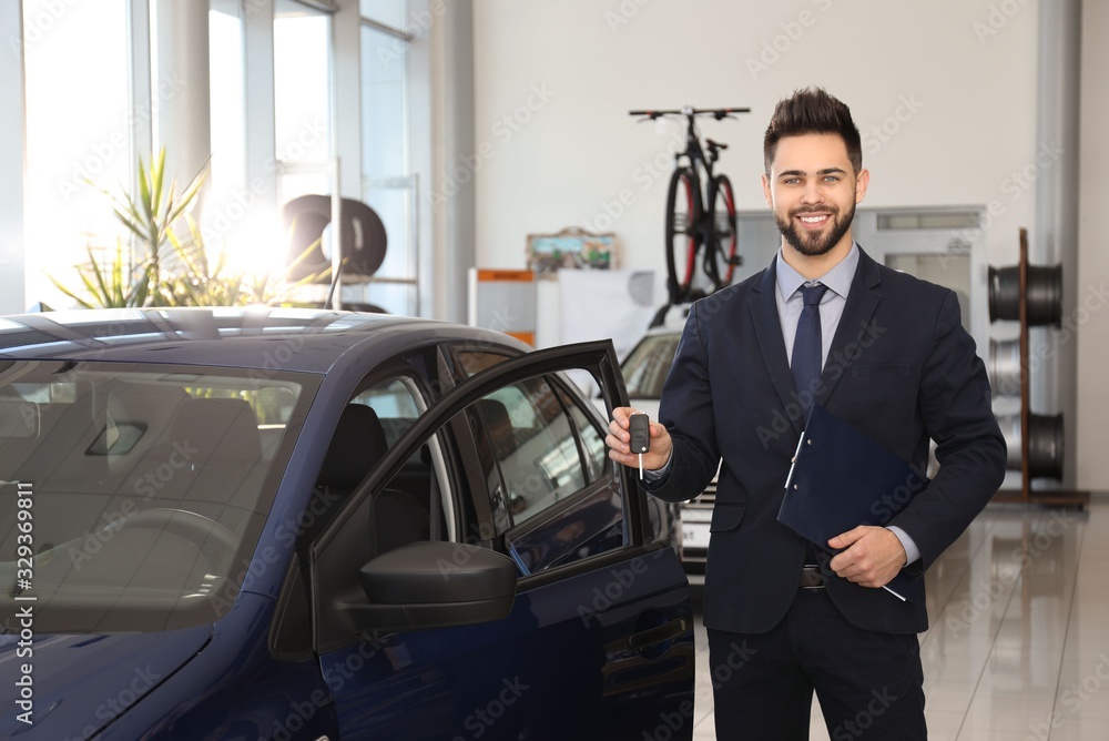 Young salesman with key and clipboard near car in dealership Young salesman with key and clipboard near car in dealership