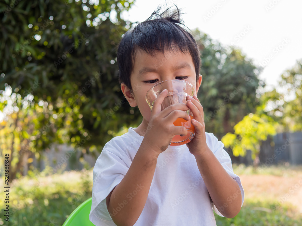 Asian little child boy drinking orange juice from glass outdoor nature background at home. Vitamin C nutrition for healthy concept. Asian little child boy drinking orange juice from glass outdoor nature background at home. Vitamin C nutrition for healthy concept.
