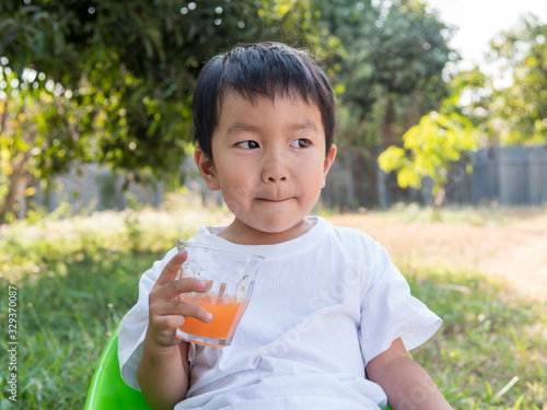 Asian little child boy holding glass of orange juice with smiling happy face outdoor nature background at home. Vitamin C nutrition for healthy concept.