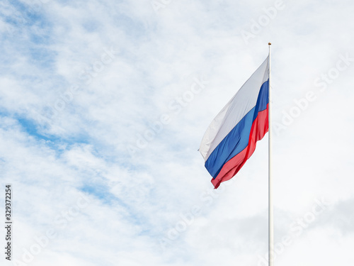 National Russian flag waving on cloudy blue sky background.