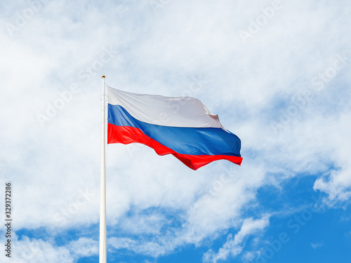 National Russian flag waving on cloudy blue sky background.