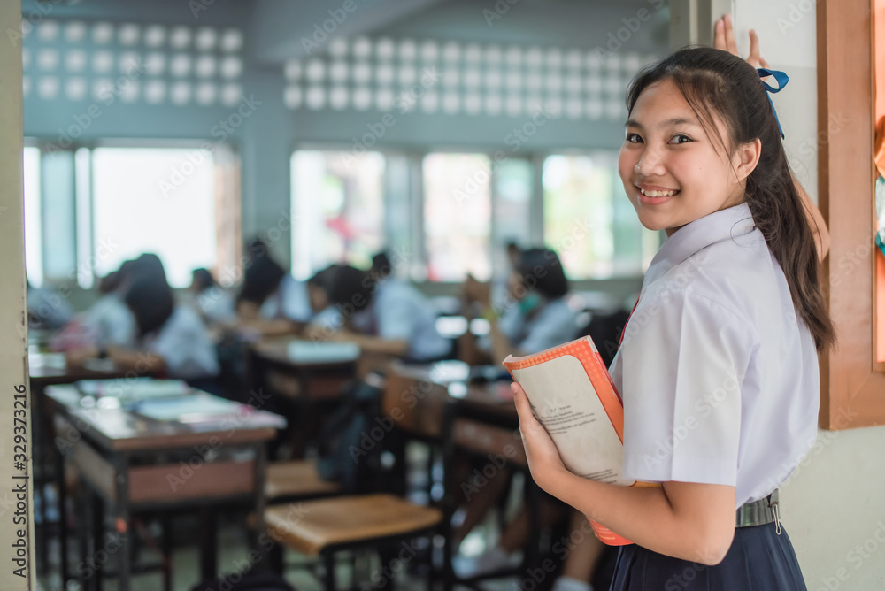An Asian female high school student in white uniform is turning her face and smiling while walking into the classroom. An Asian female high school student in white uniform is turning her face and smiling while walking into the classroom.