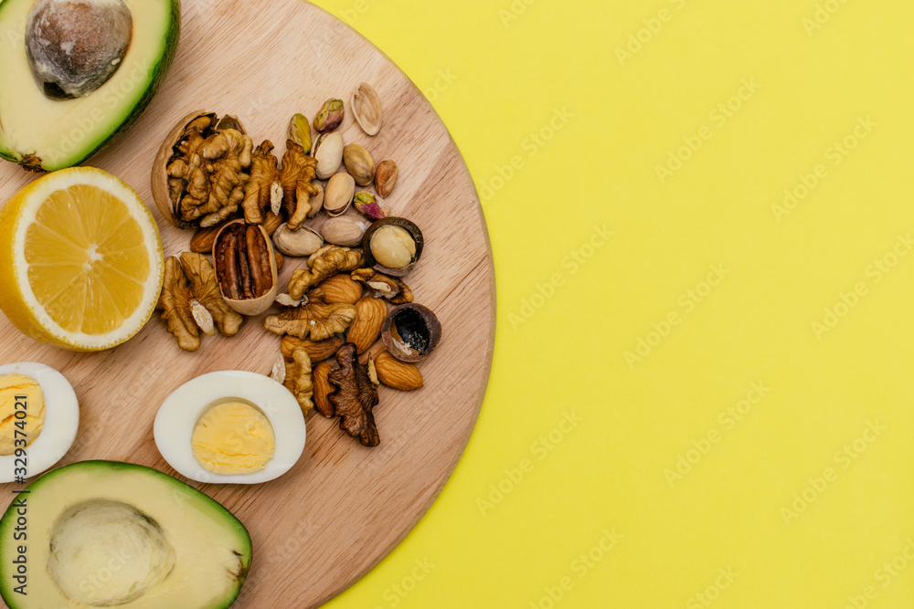 Flat lay ketogenic diet. Аvocado,eggs,lemon,nuts on the wooden cutting board on the yellow background. Concept of healthy food.Copy space for mock up Flat lay ketogenic diet. Аvocado,eggs,lemon,nuts on the wooden cutting board on the yellow background. Concept of healthy food.Copy space for mock up