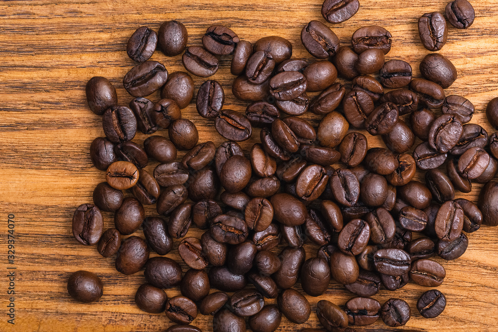 Fototapeta premium Freshly roasted coffee beans. Background of roasted coffee beans scattered on a wooden table.