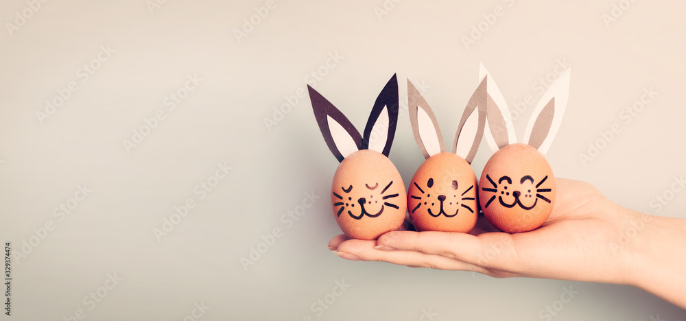 Three painted smiling Easter eggs bunnies on woman's hand - obrazy, fototapety, plakaty 