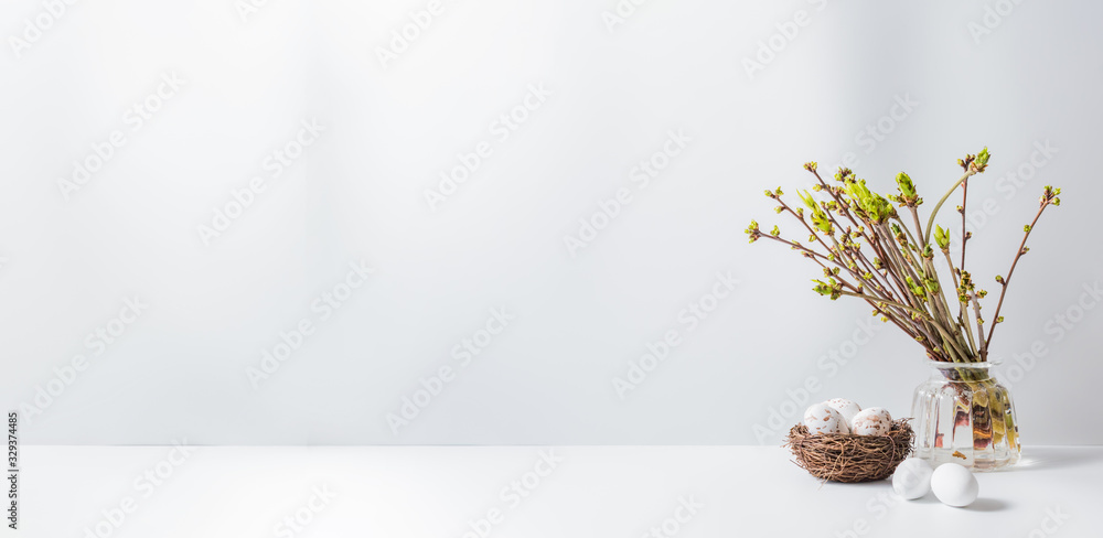 Home interior with easter decor. Green buds on branches in a glass vase, easter eggs on a light background
