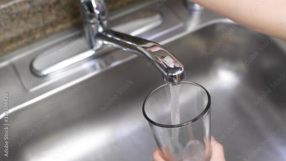 Female hand opening faucet and pouring water in glass on kitchen Female hand opening faucet and pouring water in glass on kitchen