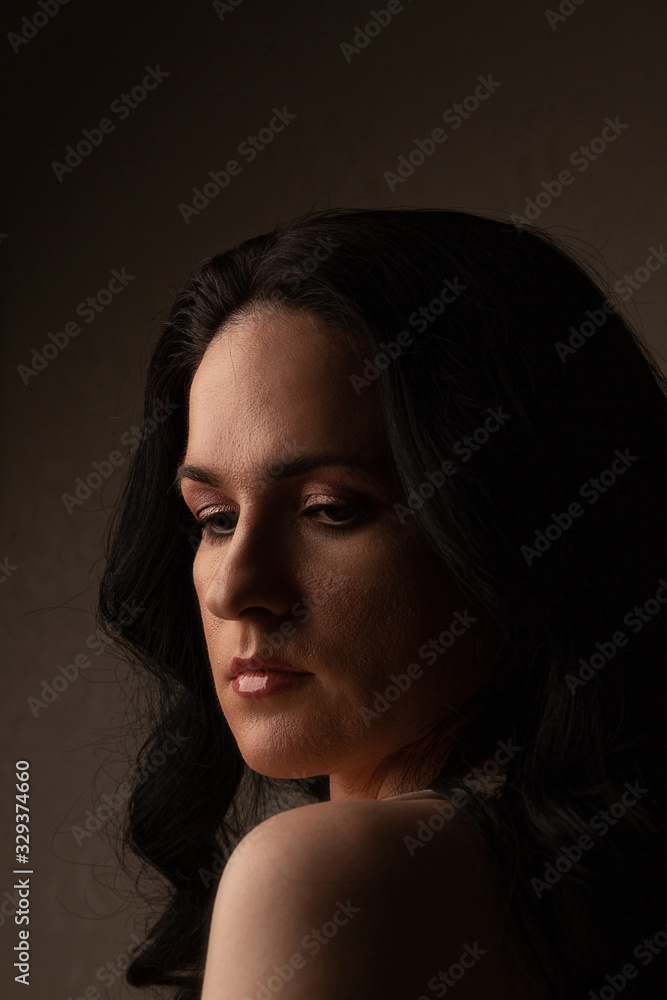 Sad woman with long curly hair posing in the shadow Sad woman with long curly hair posing in the shadow