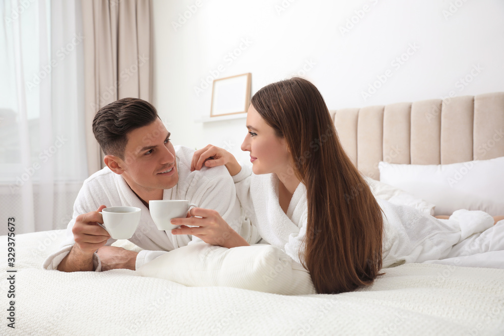 Happy couple in bathrobes with coffee on bed at home Happy couple in bathrobes with coffee on bed at home