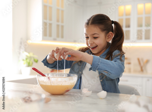 Cute little girl cooking dough at table in kitchen