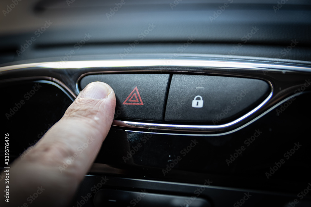 A finger pressing a hazard warning light on the interior of a car