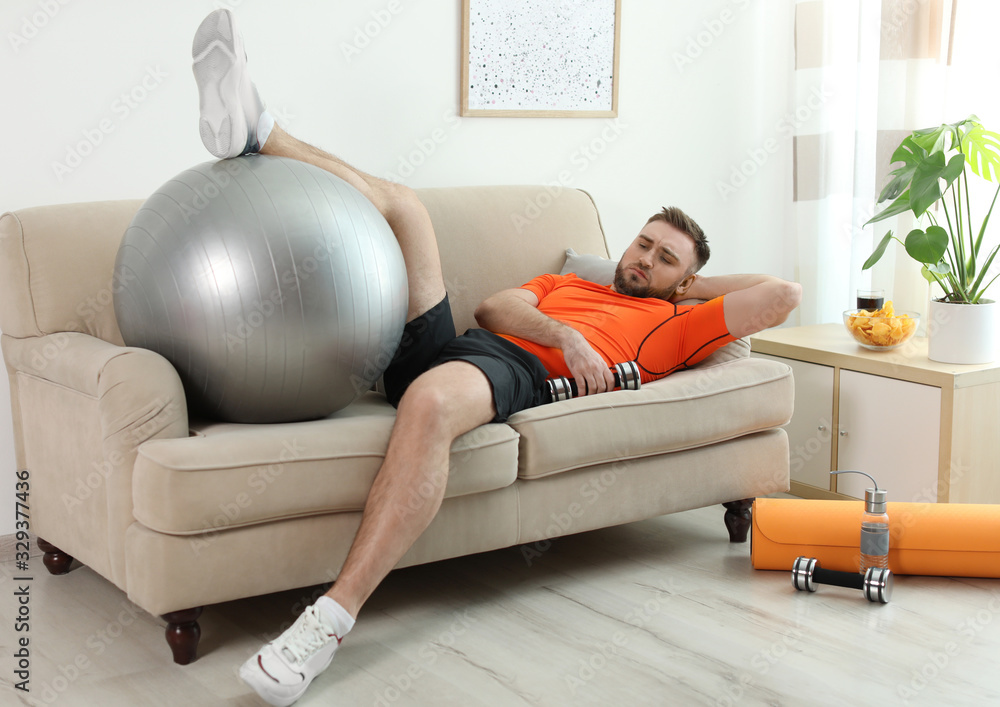 Lazy young man with sport equipment on sofa at home Stock-Foto | Adobe Stock