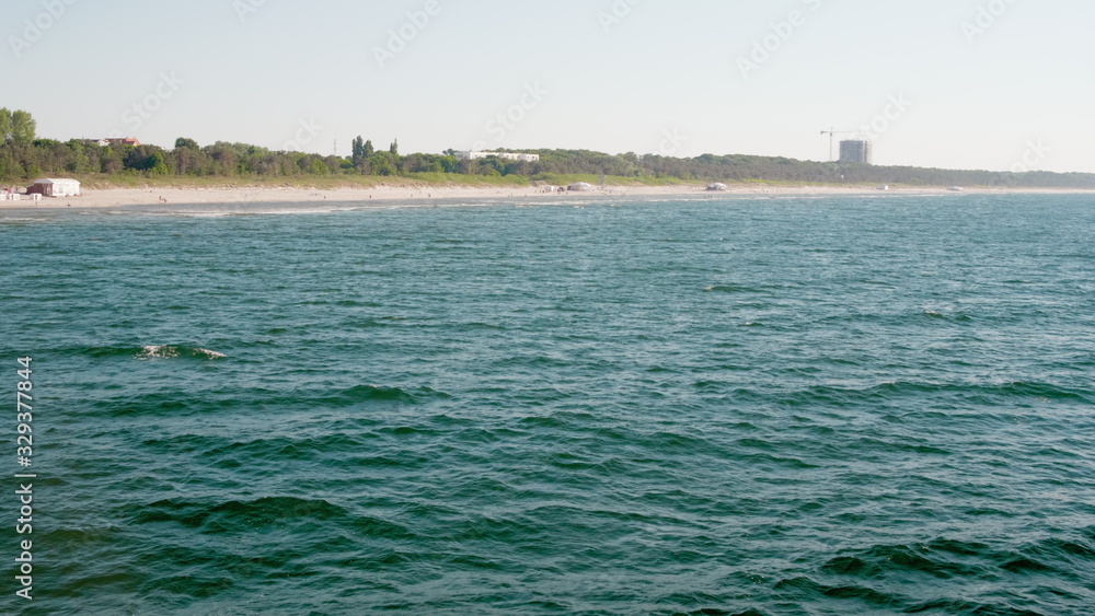 View from Sea on Beautiful Blue Water with Waves and Sand Beach with Forest and Buildings View from Sea on Beautiful Blue Water with Waves and Sand Beach with Forest and Buildings