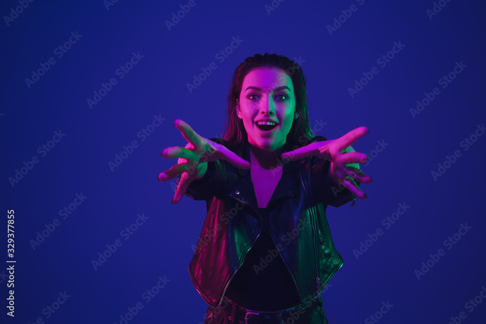 Taking on something. Caucasian woman's portrait isolated on blue studio background in neon light. Beautiful female model. Concept of human emotions, facial expression, sales, ad. Trendy colors.