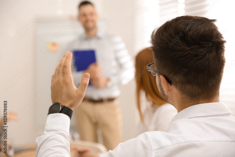 Young man raising hand to ask question at business training in conference room Young man raising hand to ask question at business training in conference room