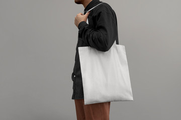 Urban mockup of tote bag. Men holding black cotton tote bag on a wall background. Template can be used for you design 