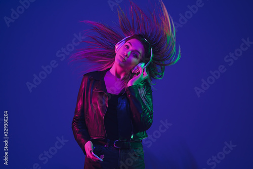 Dancing, hairs flying. Caucasian woman's portrait isolated on blue studio background in neon light. Beautiful female model. Concept of human emotions, facial expression, sales, ad. Trendy colors.