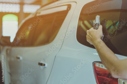 Close up to hand of male worker use wet newspapers to clean the glass part of the car. Selective focus on newspaper