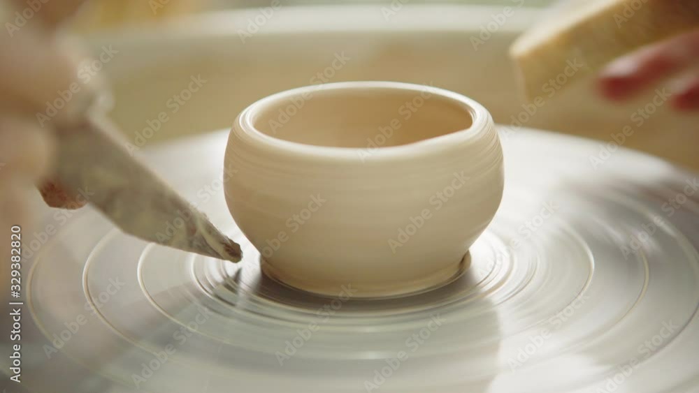 Closeup shot of hands of two ceramic artists using wooden knife and wet sponge while making clay pot on pottery wheel together Closeup shot of hands of two ceramic artists using wooden knife and wet sponge while making clay pot on pottery wheel together