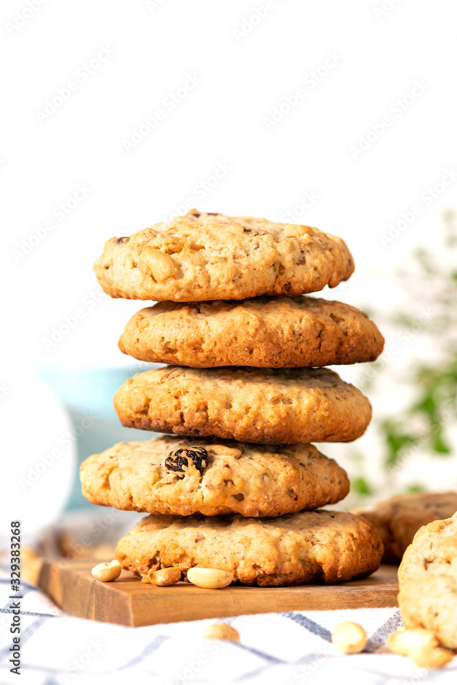 Homemade oat cookies with peanuts and raisins on the kitchen table, white background, free space for text. Stack of oatmeal cookies close-up, copy space.
