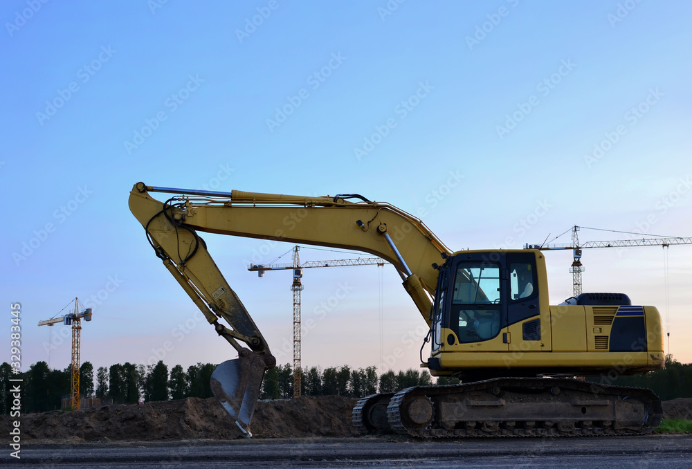 Excavator at a construction site on sunset background. Road repair, asphalt replacement. Digging the ground for the foundation and construction of a new build. Small sharpness, possible granularity Excavator at a construction site on sunset background. Road repair, asphalt replacement. Digging the ground for the foundation and construction of a new build. Small sharpness, possible granularity