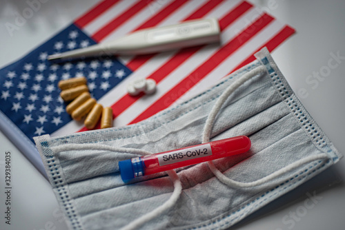 Capsules, pills and thermometer on flag of USA background. Blood test SARS-CoV-2 tube on medical mask. Coronavirus treatment concept.